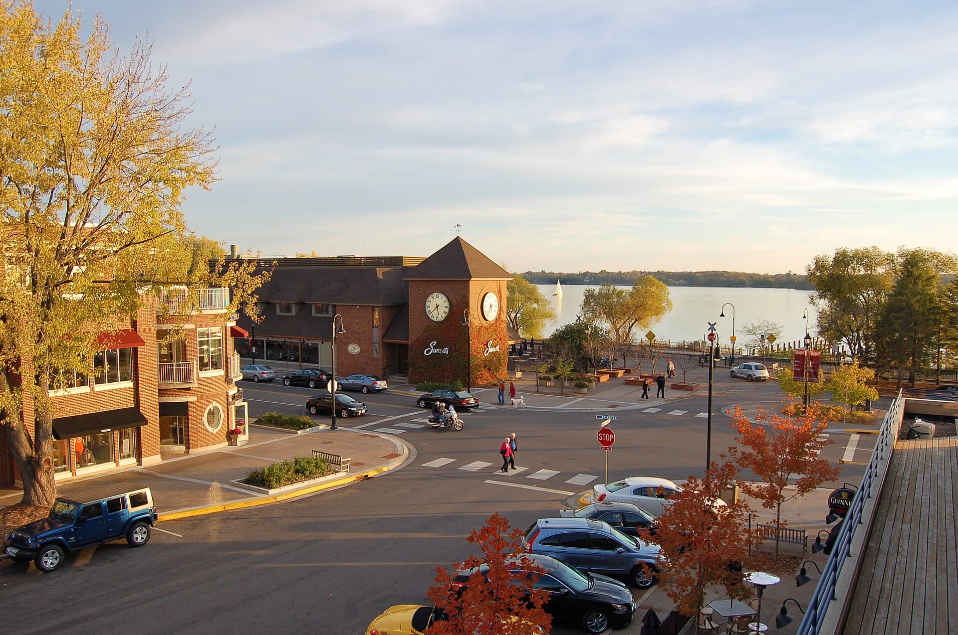 Downtown Wayzata at golden hour — brick storefronts and the landmark Wayzata clock tower with Lake Minnetonka in the background